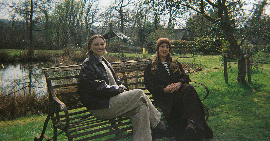 Estée Lalonde and Natalie Cassidy sitting on a bench smiling Generated with AI